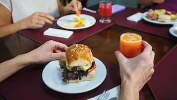 Una mesa de comedor con una comida que incluye una hamburguesa, un vaso de jugo de naranja y un plato de fruta.