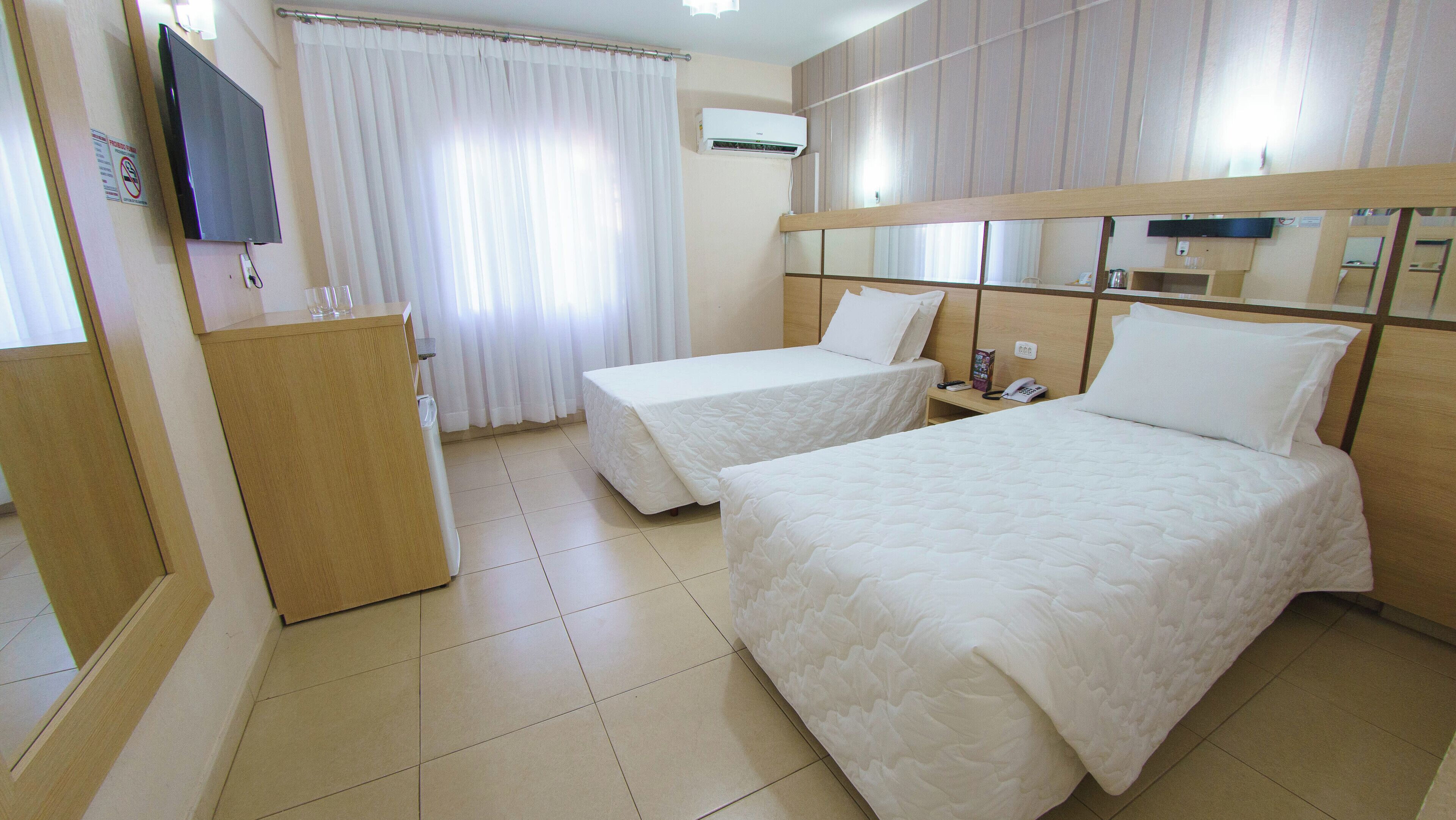 Une chambre d’hôtel avec deux lits, un bureau, une chaise, un téléviseur et un appareil de climatisation.