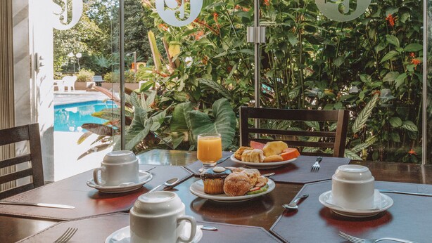 A breakfast table with plates of food, cups, and a glass of orange juice.