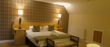 A hotel room with a large bed, two bedside lamps, a wooden nightstand, a bench, and a chair.