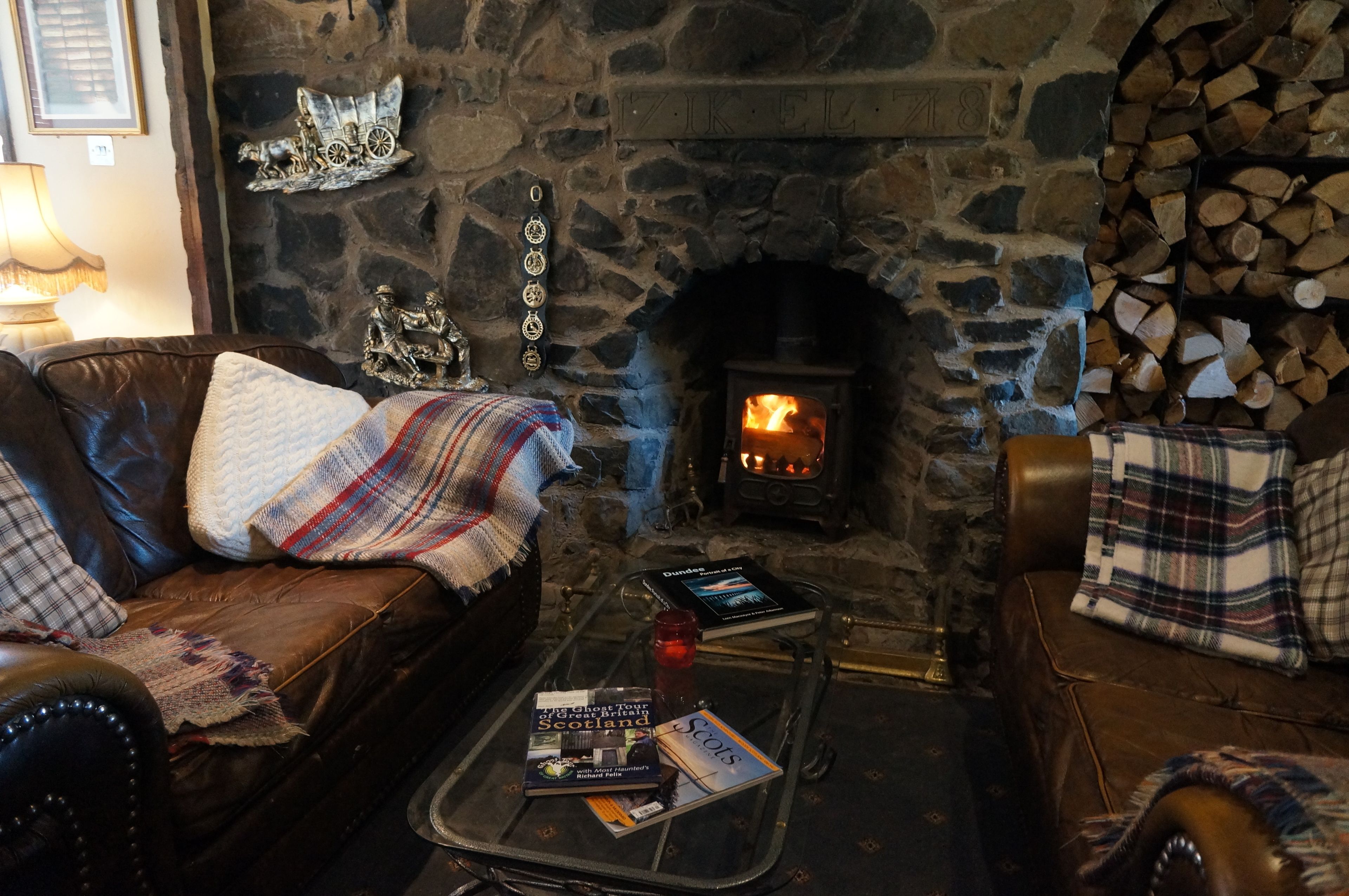 Una habitación acogedora con chimenea de piedra, sofás de cuero y una mesa de centro de vidrio con libros y una vela.