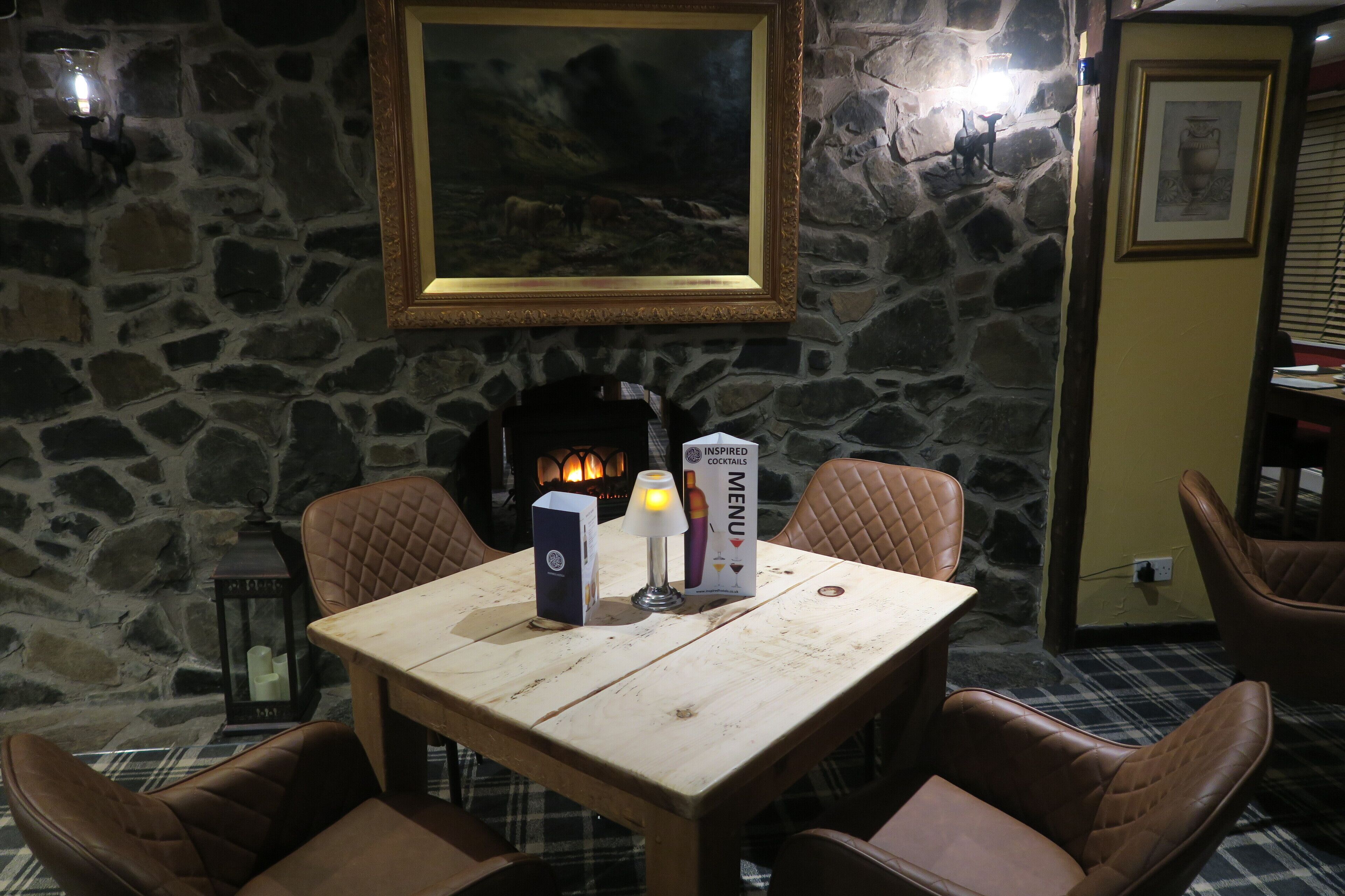 A stone wall with a framed painting, a table with a candle, a menu, and a lantern.