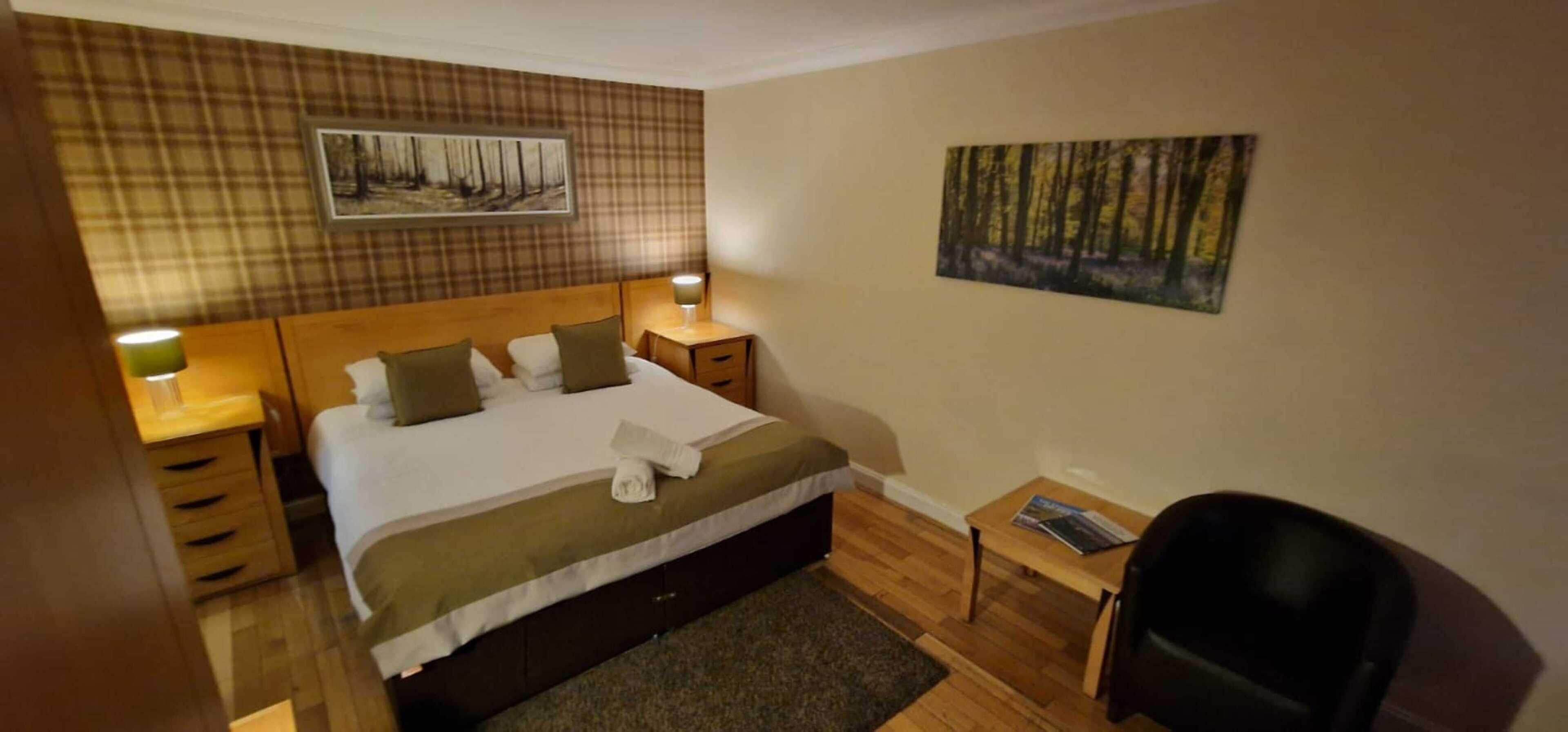 Una habitación de hotel con cama, dos mesitas de noche con lámparas, un escritorio pequeño y una silla.