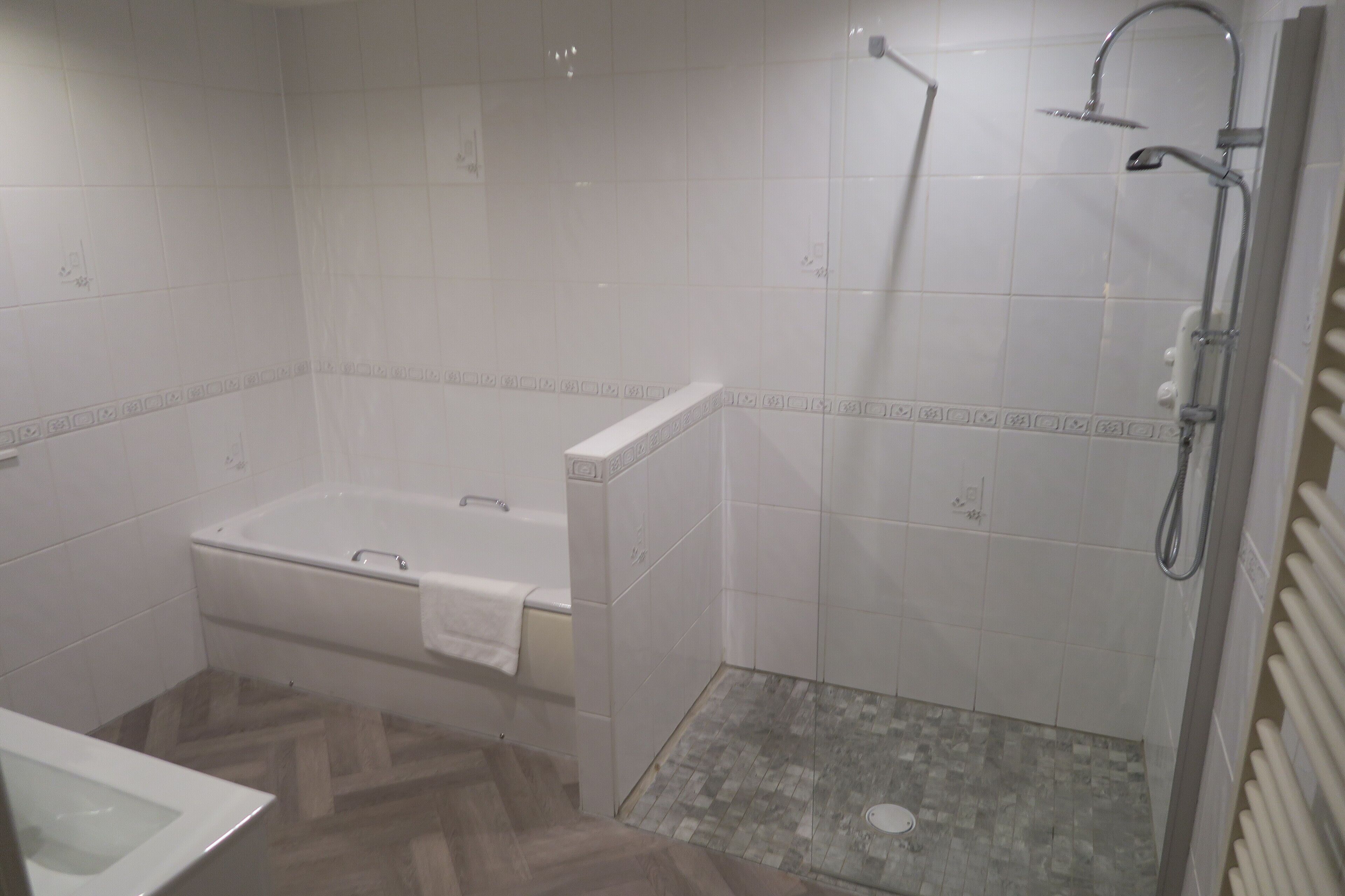 Un baño con bañera, ducha y suelo con estampado de espiga.