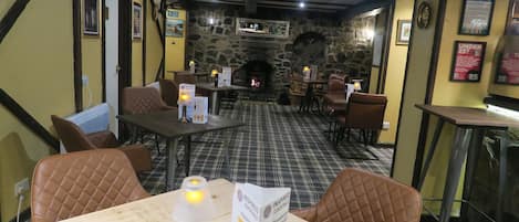 A restaurant with a stone fireplace, plaid flooring, and brown leather chairs.