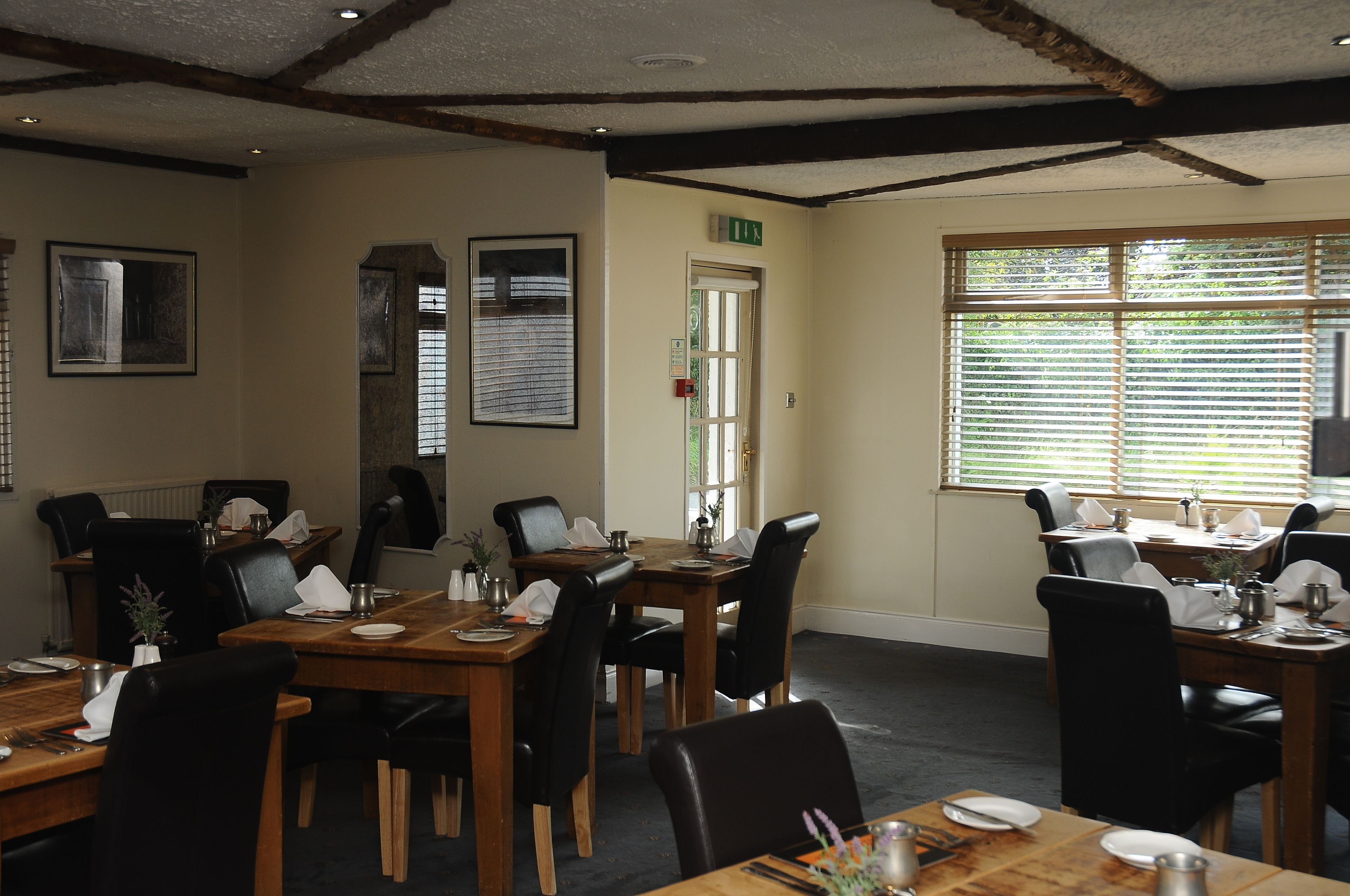 A dining area with wooden tables and black chairs, equipped with white tablecloths and silverware.