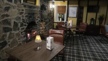 A cozy restaurant with a stone wall, wooden table, plaid carpet, and leather chairs.