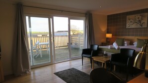 A hotel room with a bed, a desk, a chair, a table, and a view of the outdoors through a sliding door. - The Inn at Lathones (Leven)