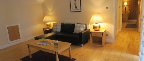 A living room with a sofa, two bedside tables with lamps, a wooden coffee table, and a framed picture on the wall.