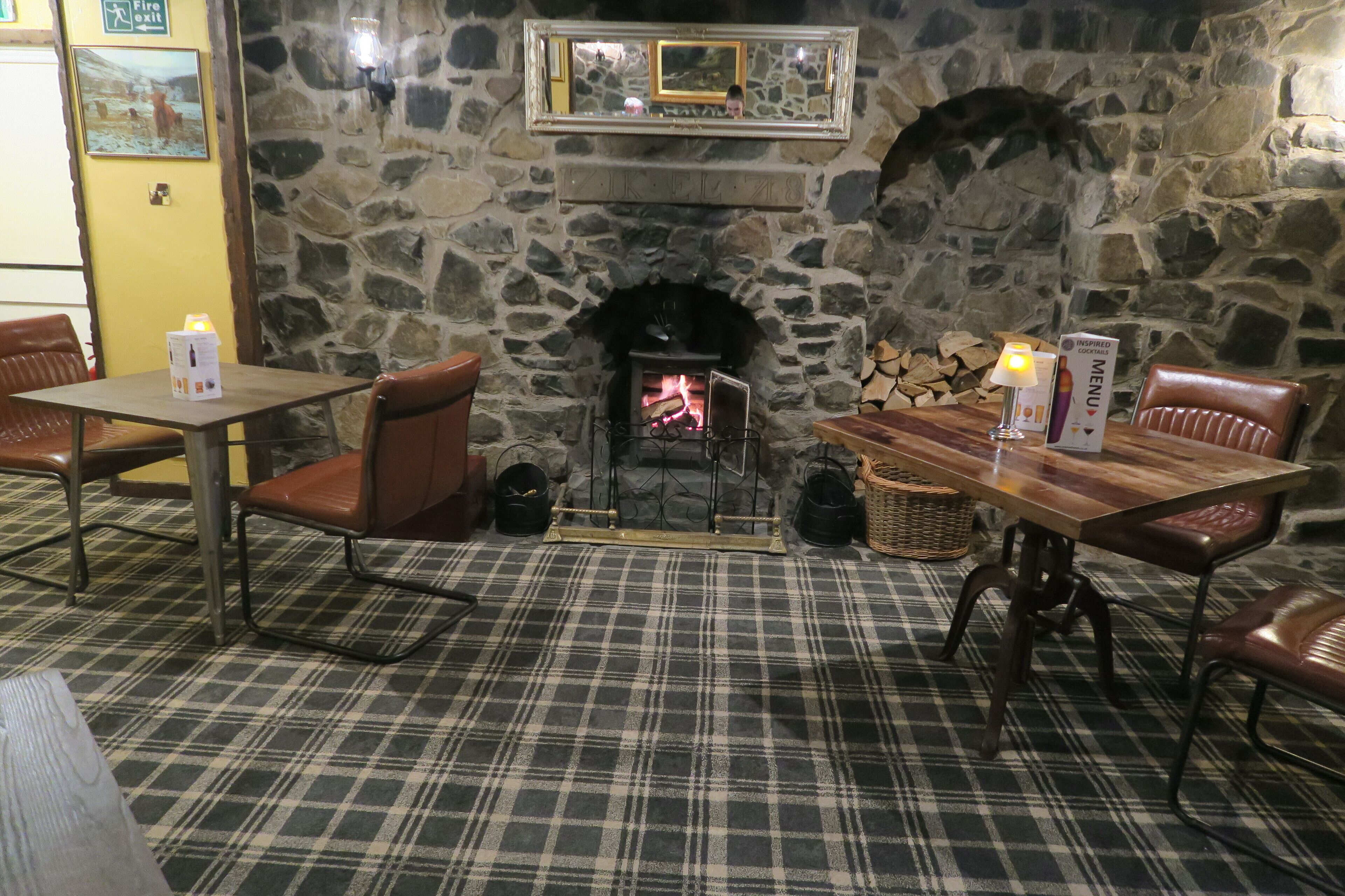 A cozy restaurant with a stone fireplace, plaid carpet, and leather chairs.