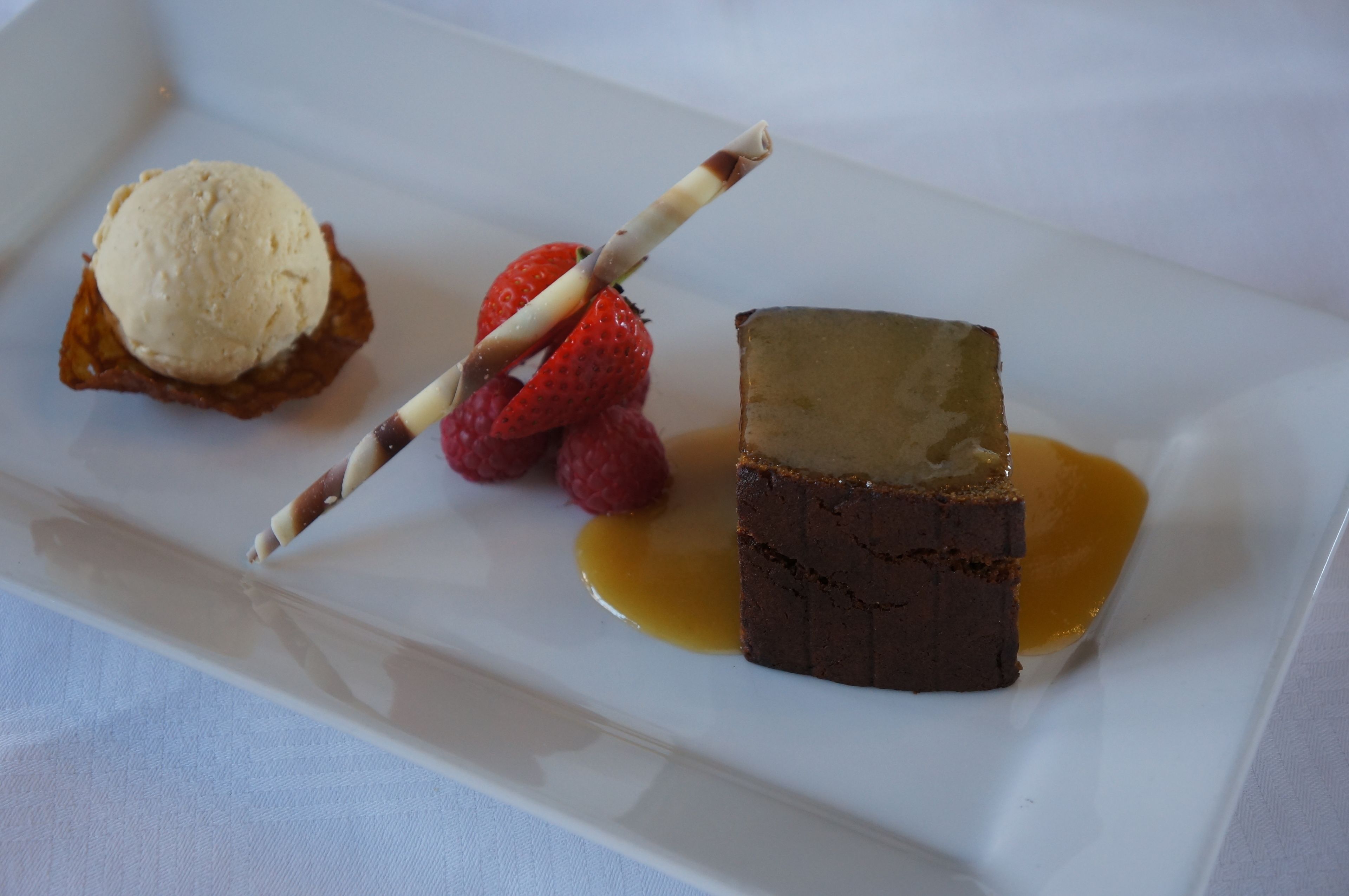 Une assiette de dessert avec une boule de glace, des fraises, des framboises et un morceau de gâteau nappé de sirop.