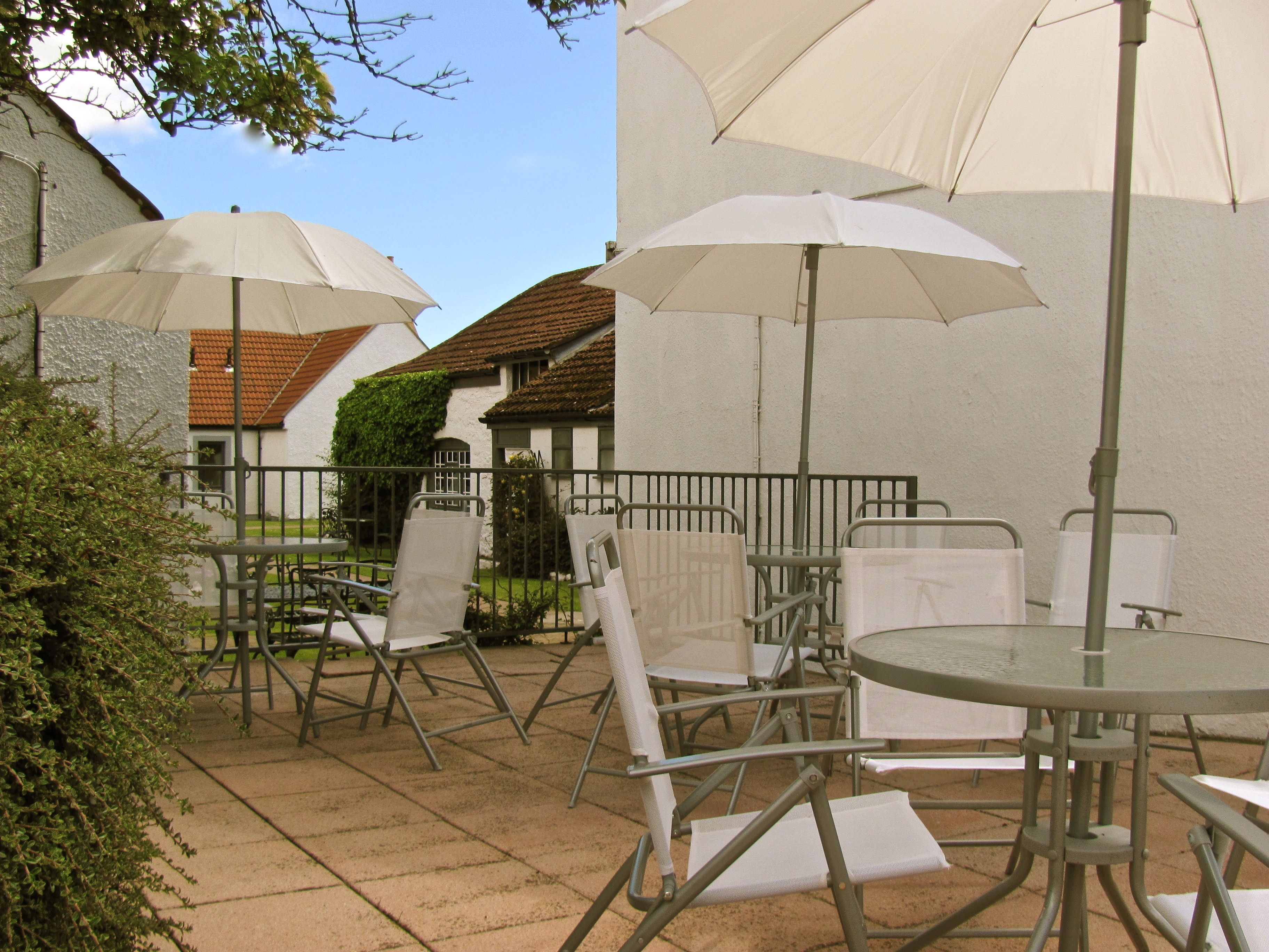 An outdoor patio area with metal tables and chairs, large white umbrellas, and a stone-tiled floor.