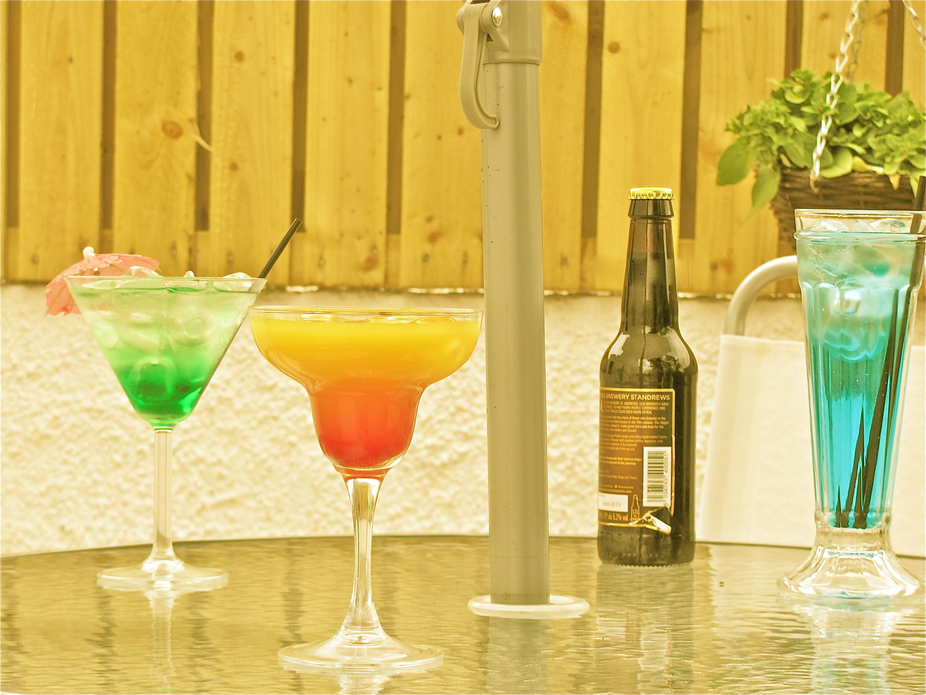 Kolme cocktail-lasia pöydällä, ja taustalla olutpullo sekä kasvi.