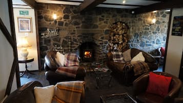A cozy lounge area with stone walls, a fireplace, leather sofas, and a small table with a lamp.