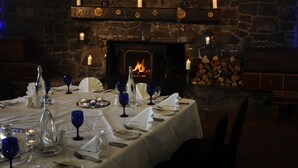 A dining table set with white tablecloth, blue wine glasses, and candles. A stone fireplace with a fire is in the background. - The Inn at Lathones (Leven)