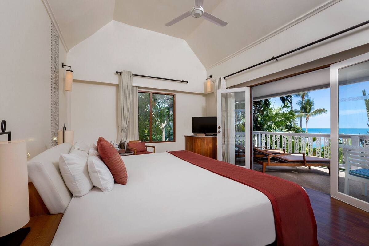 A bedroom with a bed, a TV, a desk, and a balcony with a view of the ocean.