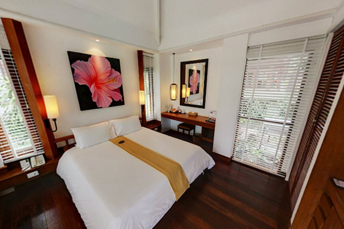 A hotel room with a large bed, a desk, a chair, a lamp, and a window with blinds.