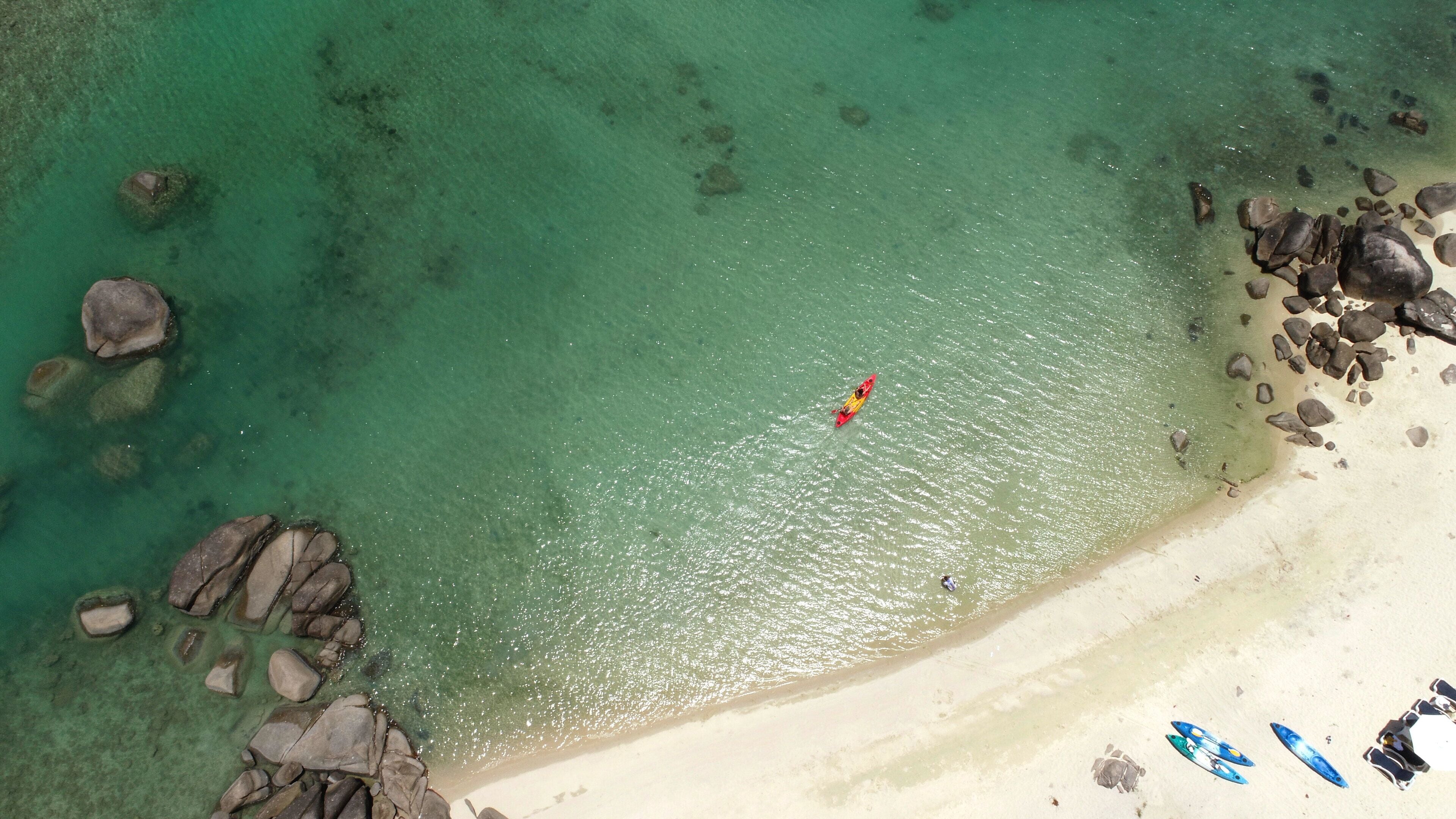 A beach with clear turquoise water, a sandy shore, and scattered rocks.