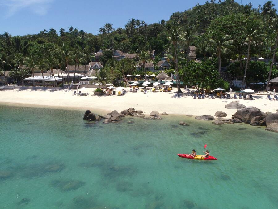 Una playa con agua turquesa cristalina, un litoral rocoso y un kayak rojo con dos personas.
