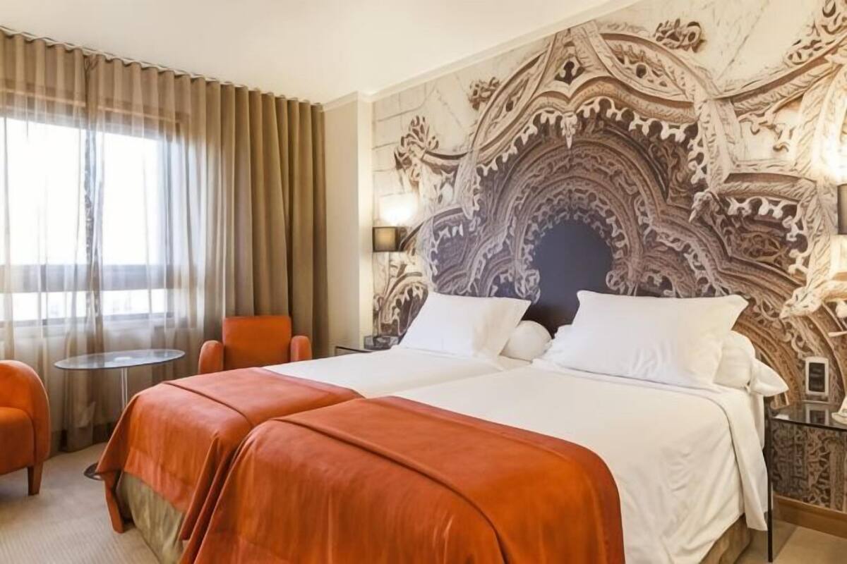 Une chambre d’hôtel avec un grand lit, deux tables de chevet, une chaise et une tête de lit décorative.