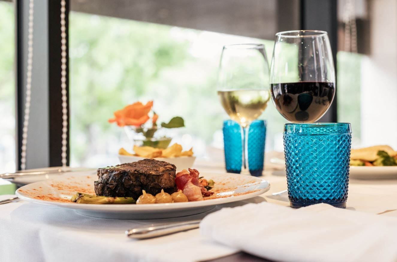Una mesa de comedor con un plato de comida, dos copas de vino y un vaso azul con textura.