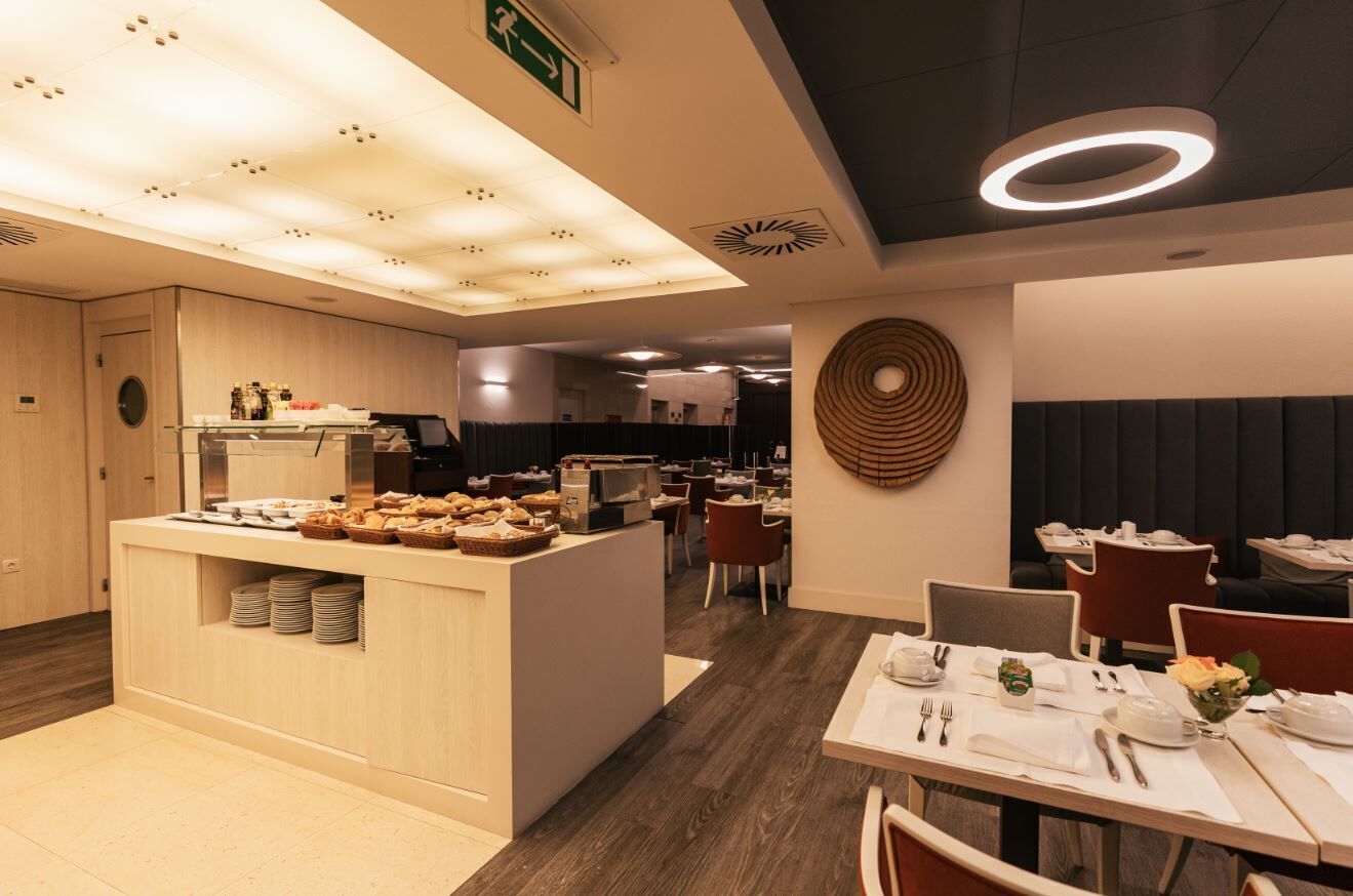 Un comedor moderno con una estación de buffet, mesas ordenadas y un elemento decorativo circular en la pared.