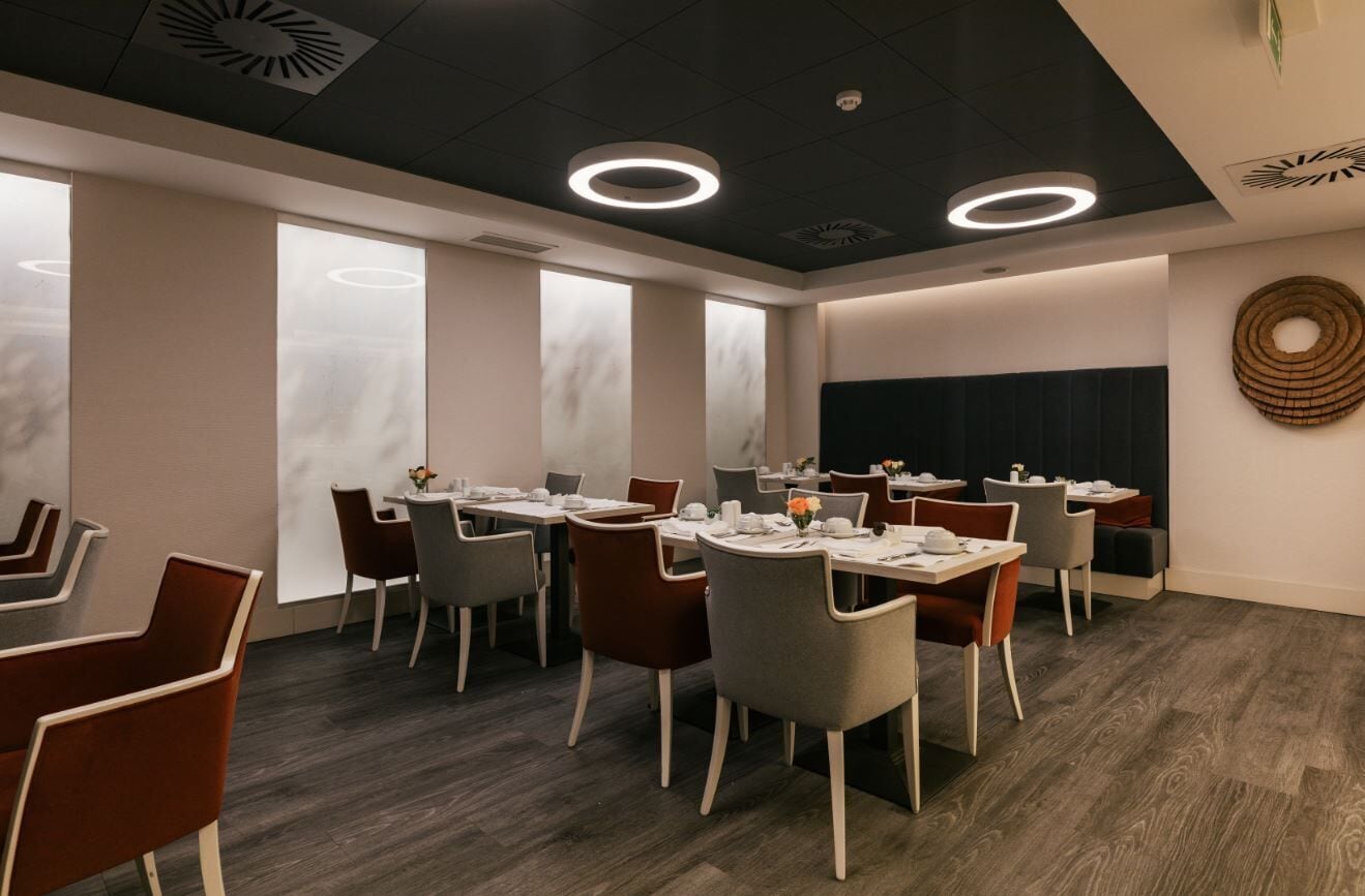 A modern dining area with round tables, chairs, and a dark ceiling with circular light fixtures.