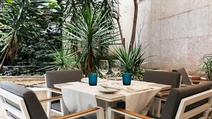 Un espace de restauration en plein air avec des tables et des chaises blanches, entouré d’une végétation luxuriante.