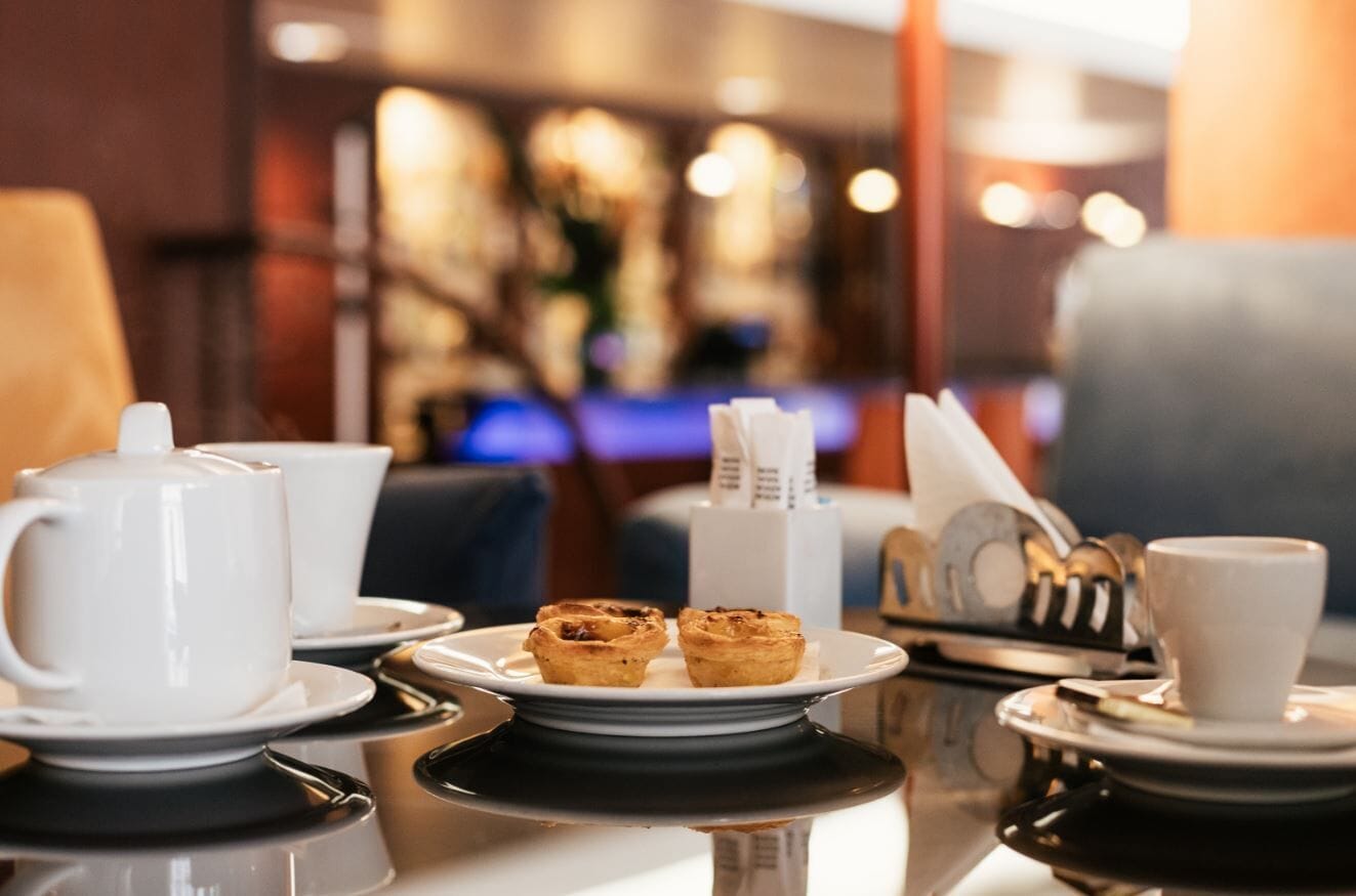 A table set with a teapot, cups, a plate with pastries, and a napkin holder.