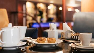 A table set with a teapot, cups, a plate with pastries, and a napkin holder.