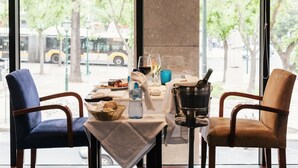 Une table dressée pour deux personnes, avec une bouteille d’eau, des verres à vin et un panier de pain.