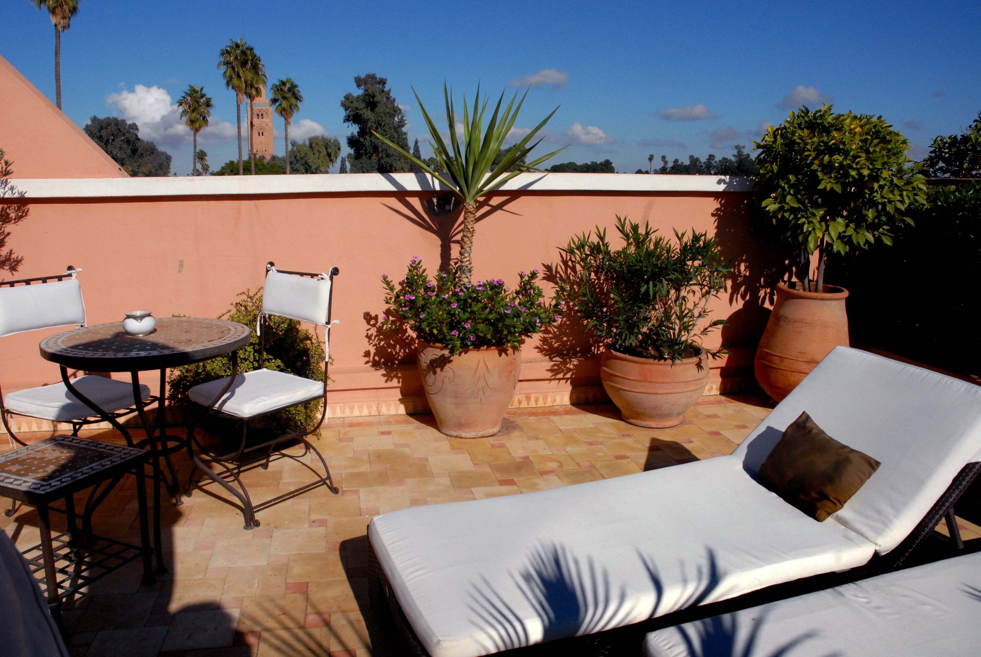 A rooftop terrace with a lounge chair, a small table, and potted plants.