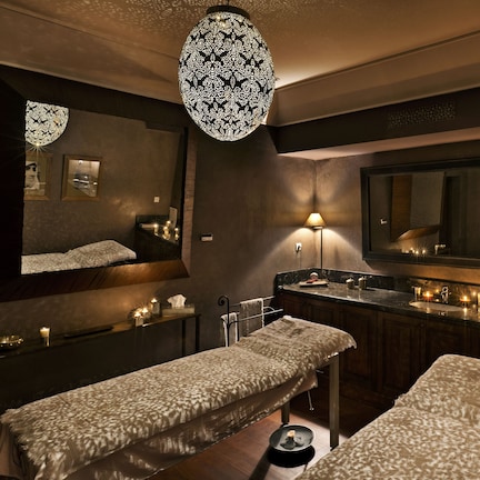 A spa room with two treatment beds, a large mirror, and a long counter with candles.