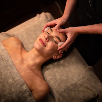 A person lying on a massage table receiving a head massage.