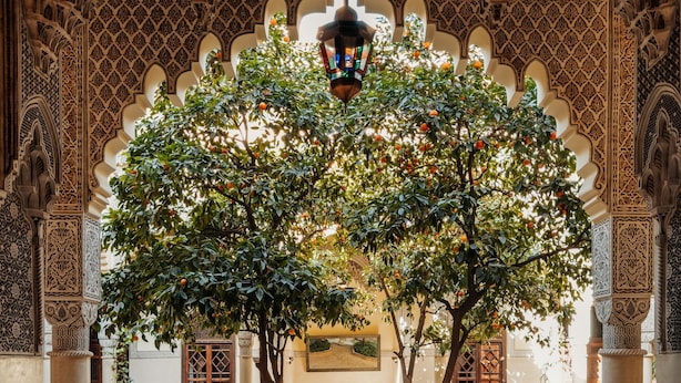 An ornate interior with intricate arches, a central tree, and a seating area with tables and chairs. - La Villa Des Orangers - Relais & Châteaux (Marrakech)