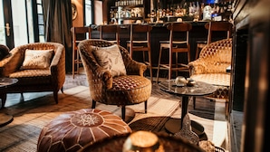 A bar area with leather armchairs, a round table, and a bar counter with bottles. - La Villa Des Orangers - Relais & Châteaux (Marrakech)