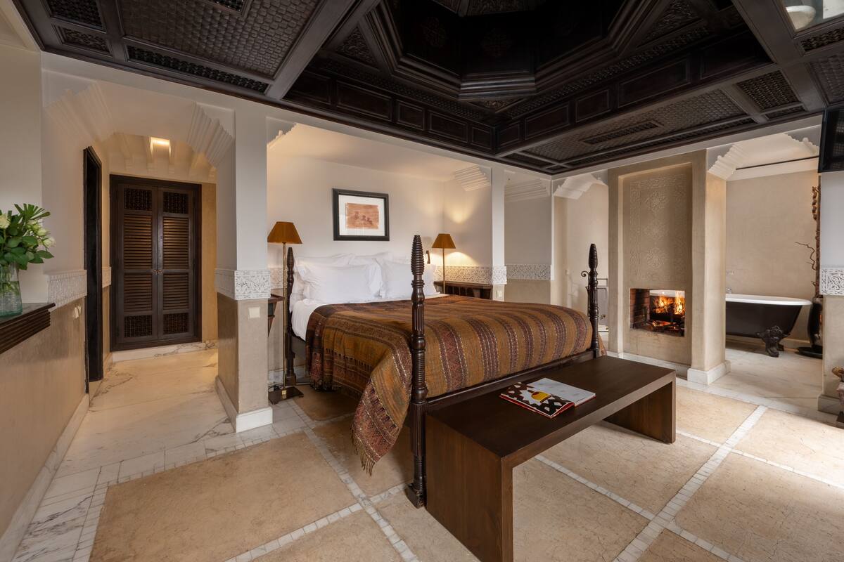 A hotel room with a large bed, a wooden coffee table, a fireplace, and a bathtub.