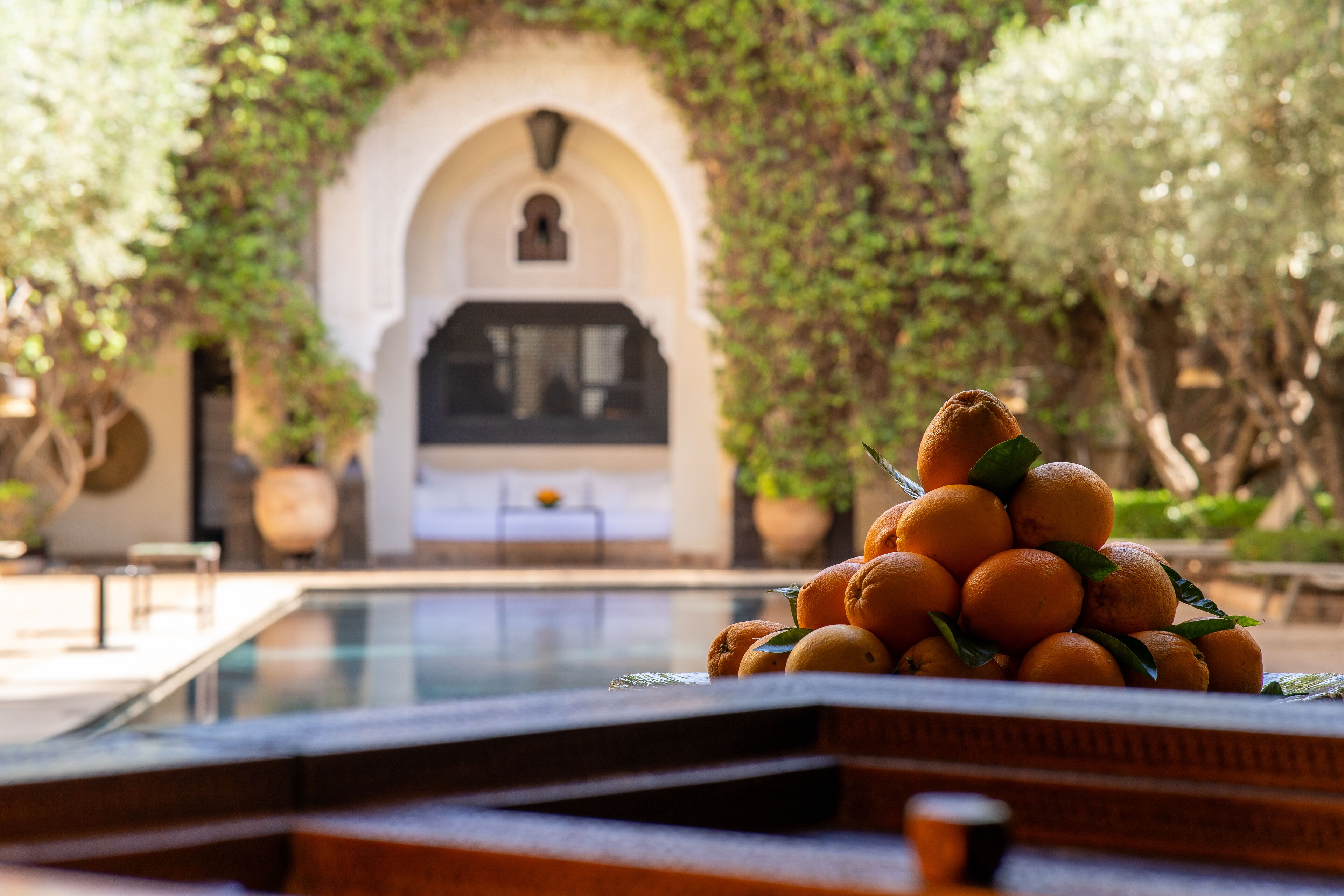 A pool area with a stack of oranges and a view of a building with an arched entrance.