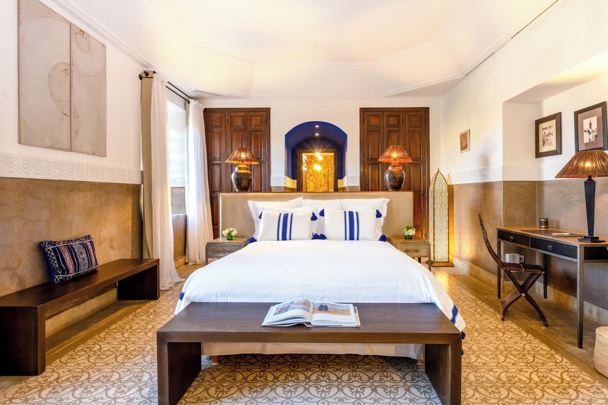 A well-lit bedroom with a large bed, bedside lamps, a desk, and a chair.