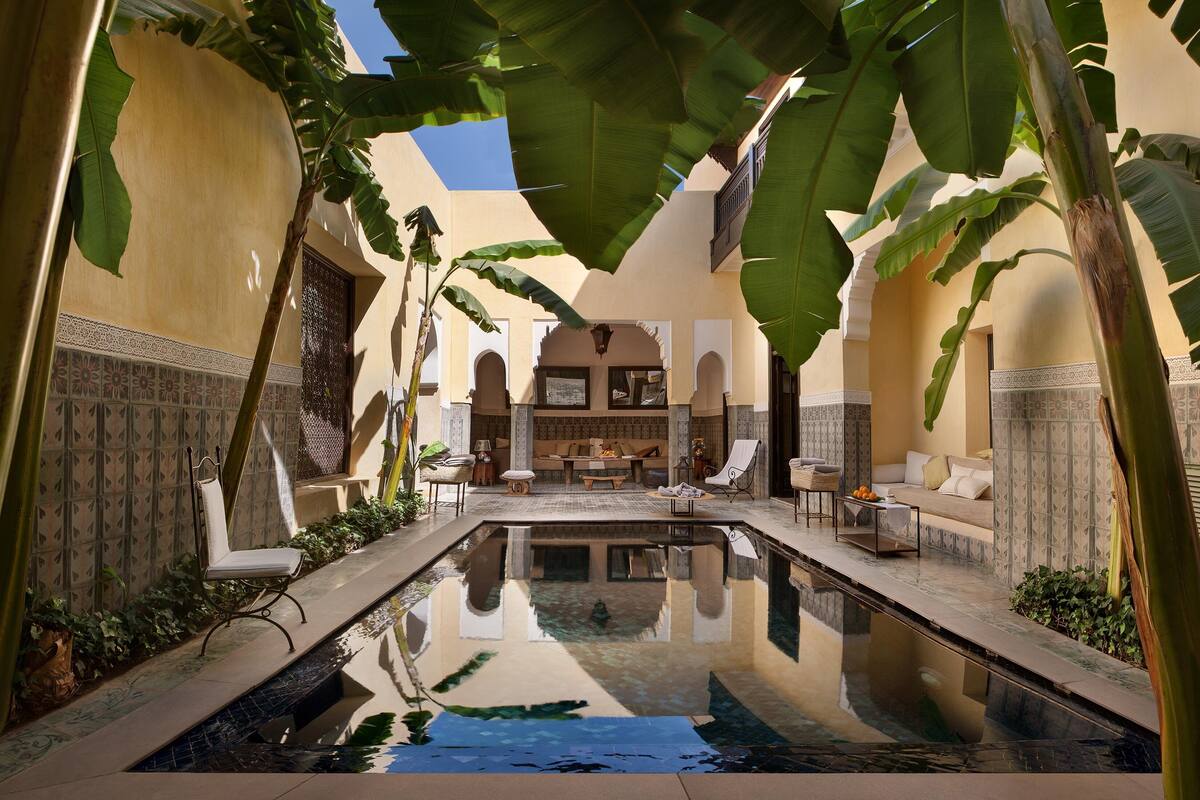 A serene indoor pool area with a central seating area, surrounded by large tropical plants and traditional Moroccan architectural elements.