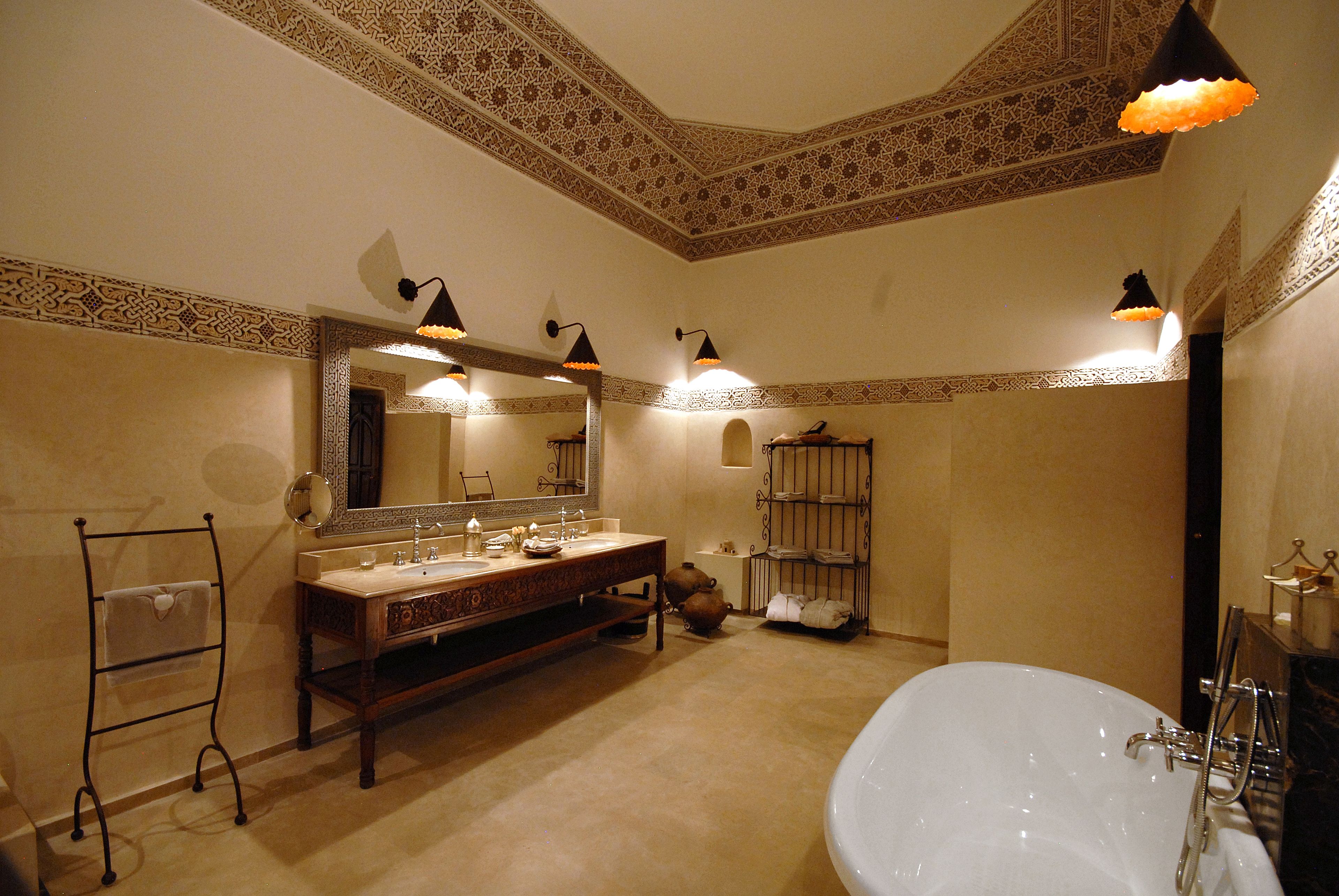 Un bany amb una banyera gran, un lavabo amb mirall i motius decoratius a les parets.