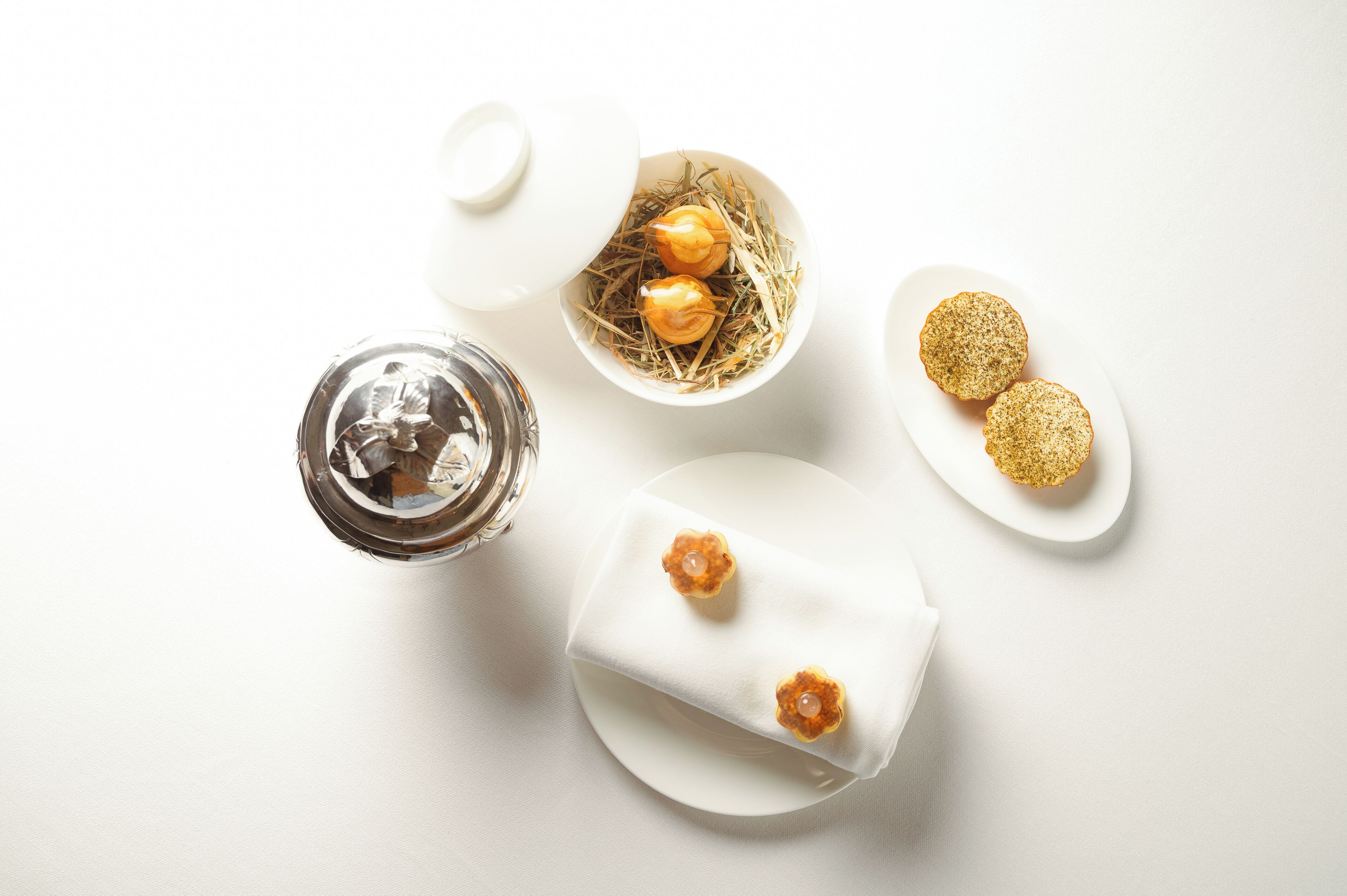 A white table with a glass of water, a bowl of eggs, and two plates of cookies.