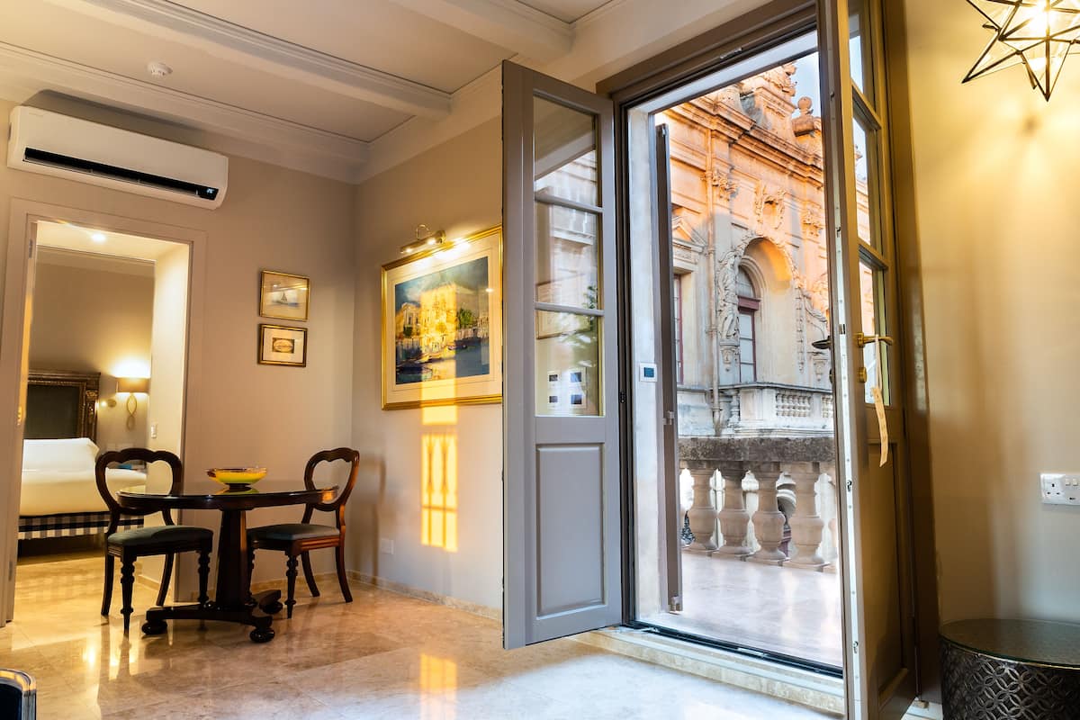Quarto de hotel com área de refeições, uma grande janela com vista para um edifício histórico e um aparelho de ar condicionado.