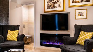 A modern living room with two grey armchairs, a flat-screen TV, and a fireplace.
