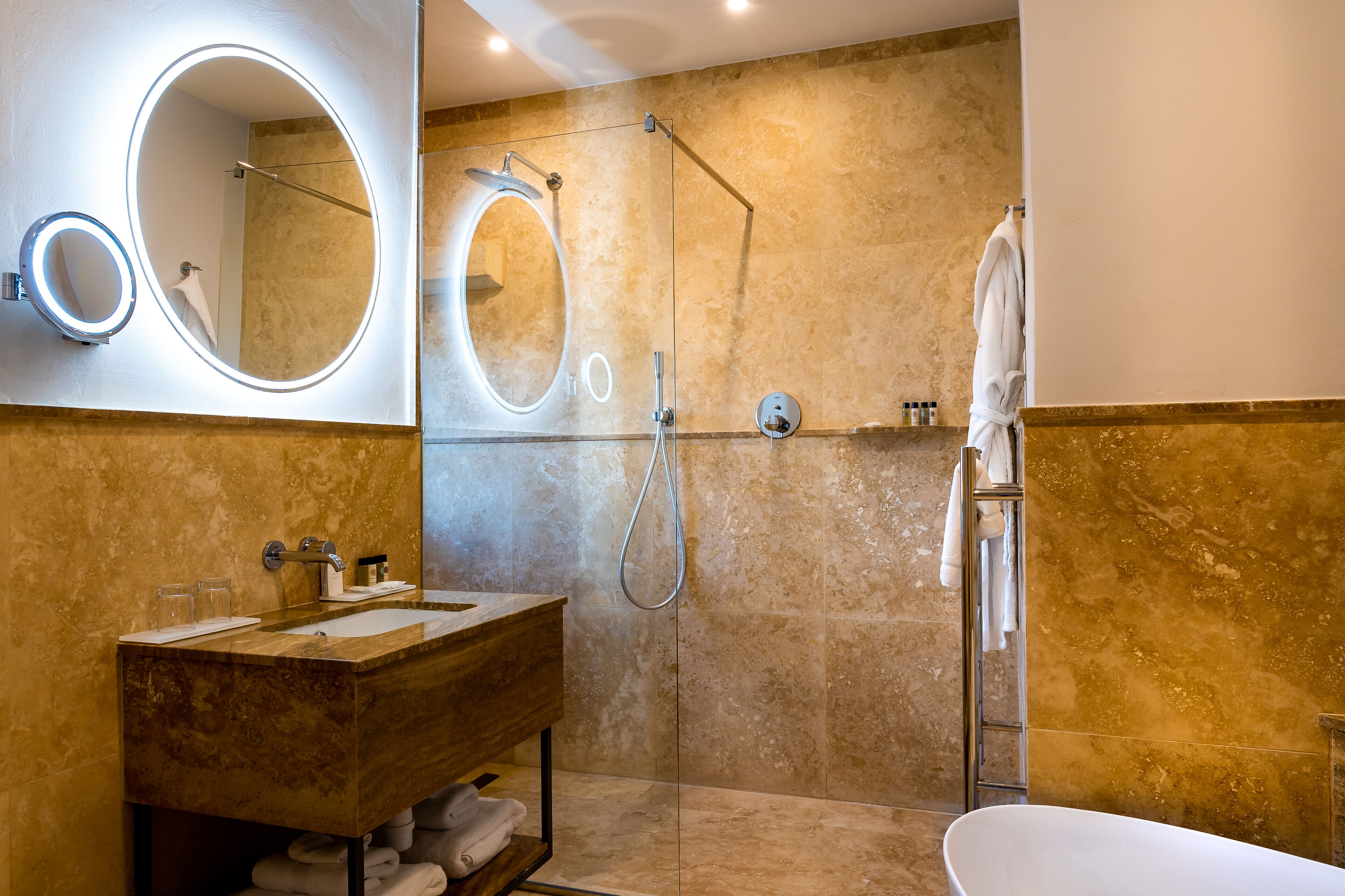 Un baño moderno con tocador de mármol, dos espejos grandes, cabina de ducha a ras de suelo y bañera.