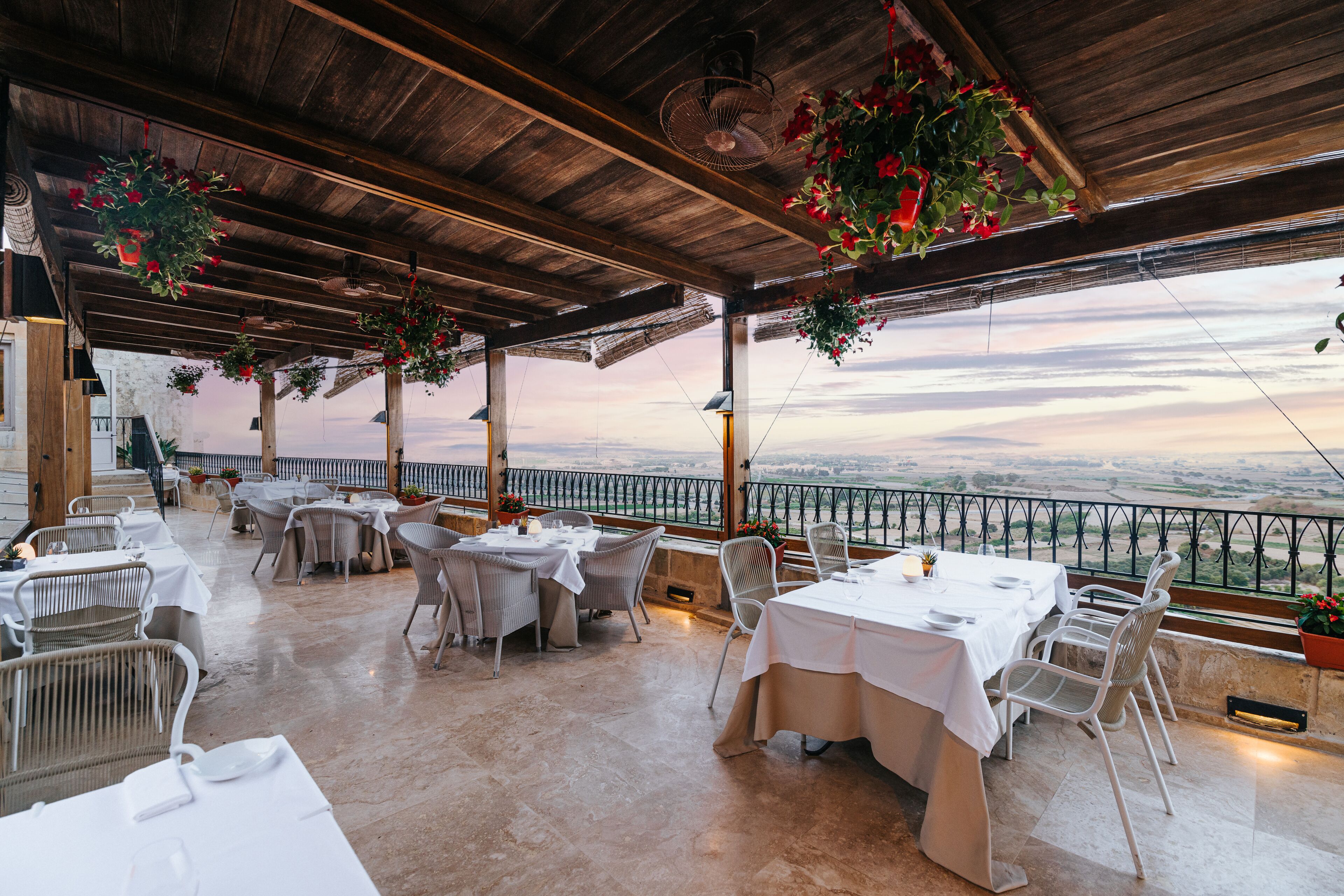 Un área de comedor al aire libre con mesas y sillas, techo de madera y plantas colgantes.