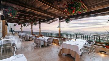 Un área de comedor al aire libre con mesas y sillas, techo de madera y plantas colgantes.