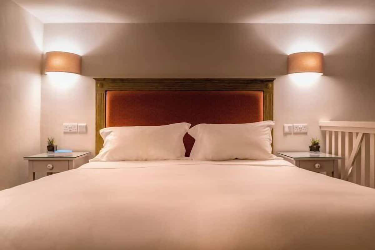 Cama bem arrumada com duas almofadas, cabeceira de madeira, mesas de cabeceira com abajures e corrimão branco.