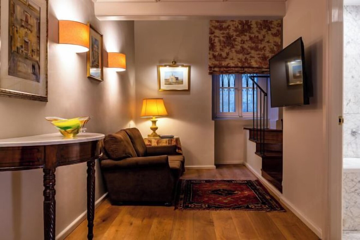 Una sala de estar con sofá, una mesa, lámpara, televisor y una escalera.