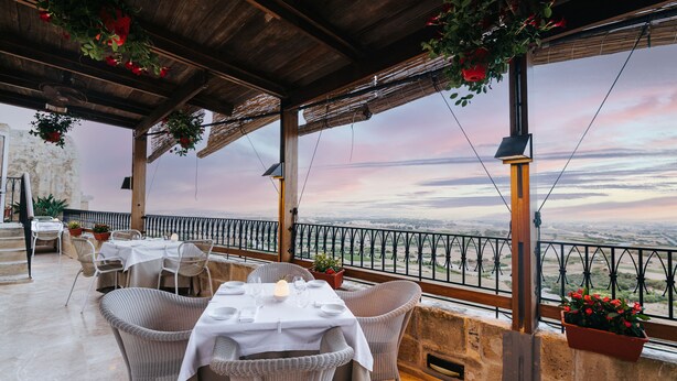 An outdoor dining area with wicker chairs and tables, a view of the landscape, and hanging red flowers.